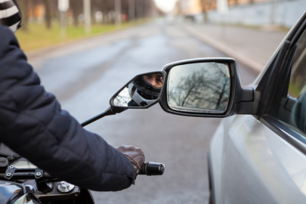 Motorcycle rider touching side mirror of a car when riding nearby on a road, close-up view
