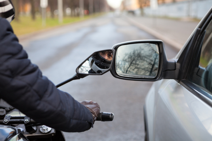 Motorcycle rider touching side mirror of a car when riding nearby on a road, close-up view