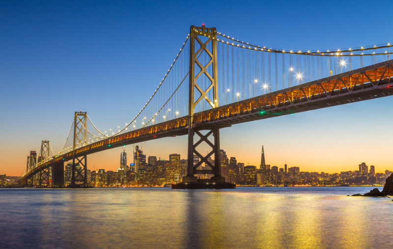 Classic panoramic view of famous Oakland Bay Bridge with the skyline of San Francisco in the background illuminated in beautiful twilight after sunset in summer, California, USA
