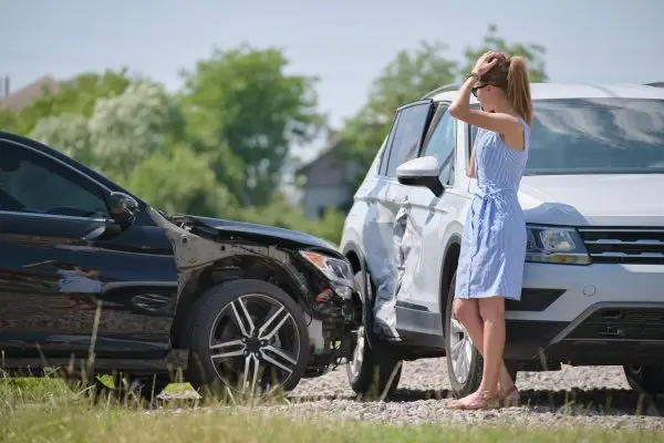 Distressed woman standing beside damaged SUV after causing a car accident on a sunny day