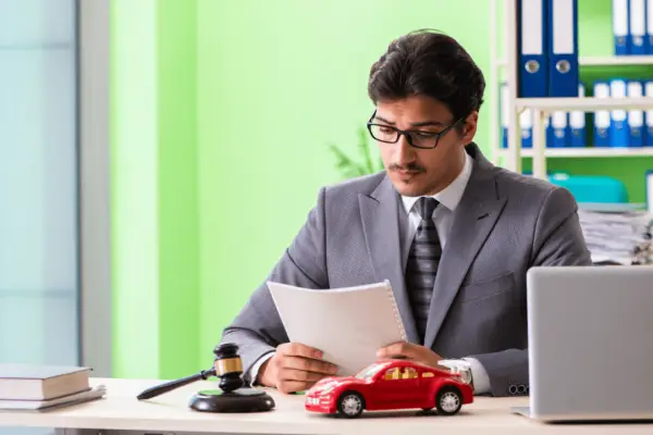 Personal injury lawyer reviewing car accident settlement timeline documents with red toy car and gavel on desk