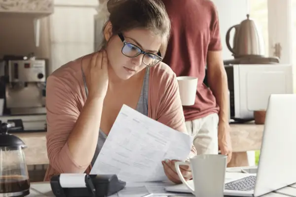 Young woman reading paperwork at kitchen table, researching how to win a car insurance claim.
