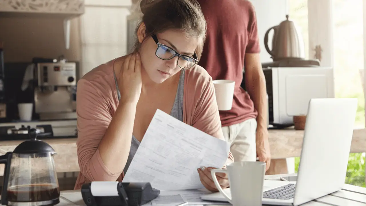 Young woman reading paperwork at kitchen table, researching how to win a car insurance claim.
