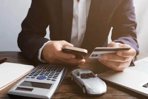 Person calculating how to maximize payout from a car accident with calculator and toy car on desk
