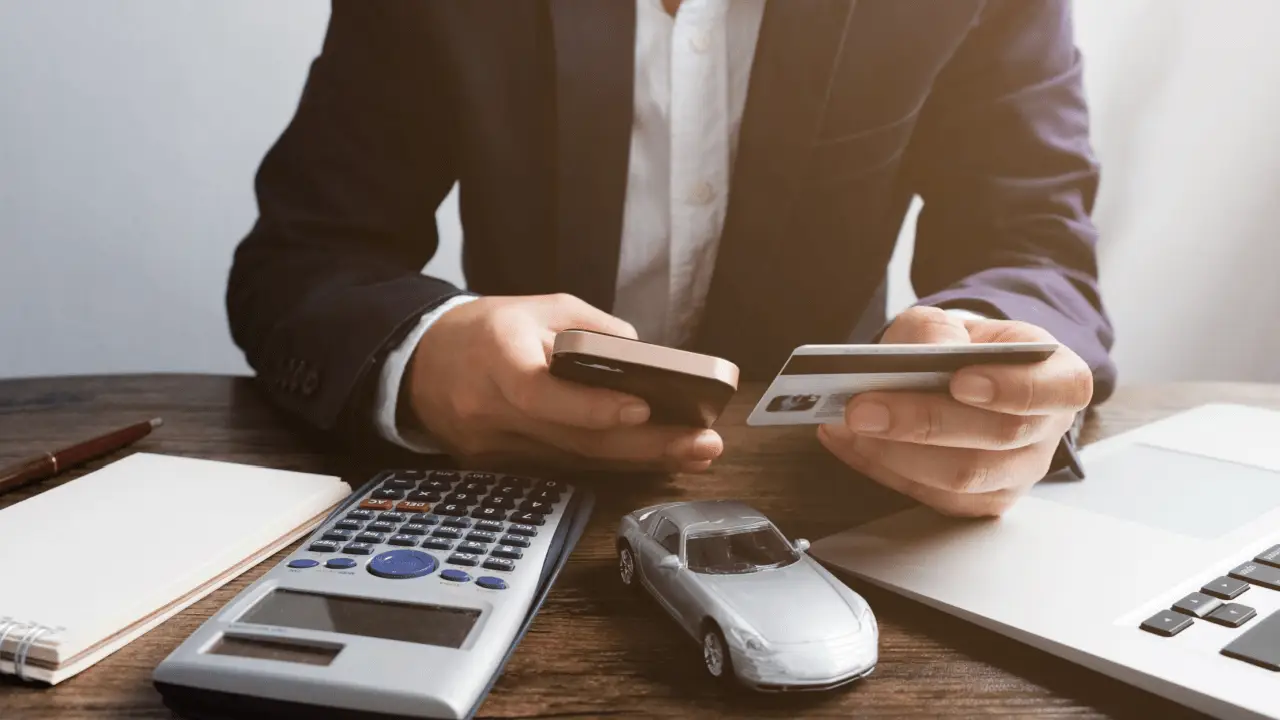 Person calculating how to maximize payout from a car accident with calculator and toy car on desk