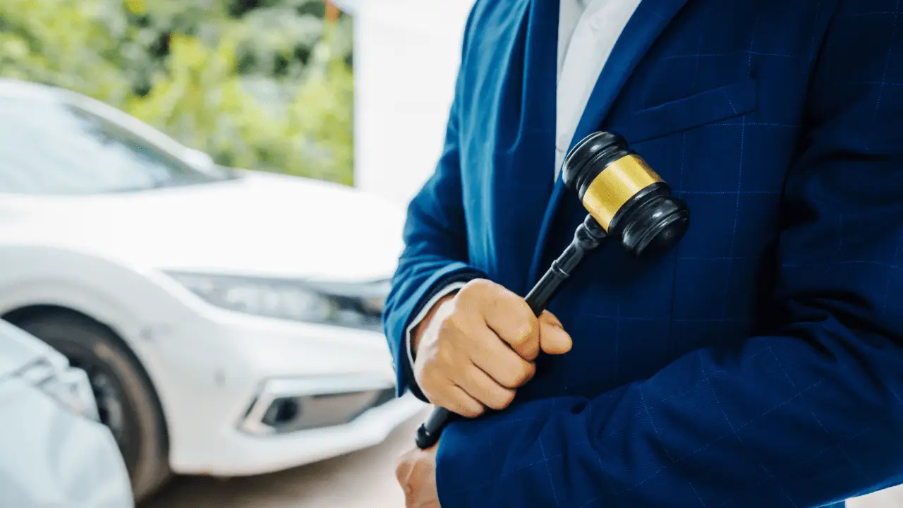 Traffic accident lawyer holding gavel with damaged white car in background after collision