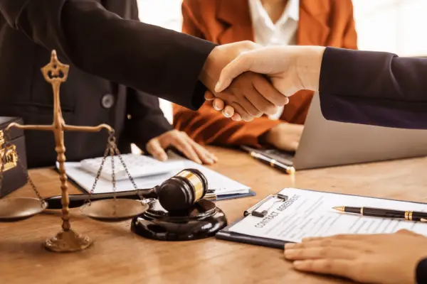 Lawyers shaking hands after discussing what is a reasonable settlement offer with scales of justice and gavel on desk