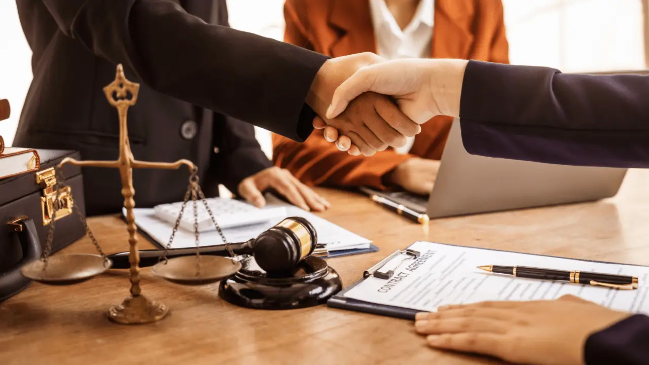 Lawyers shaking hands after discussing what is a reasonable settlement offer with scales of justice and gavel on desk