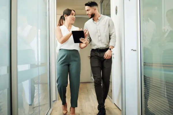 Professional woman and man in business attire walking through office corridor discussing what not to say when you hit a car after accident consultation