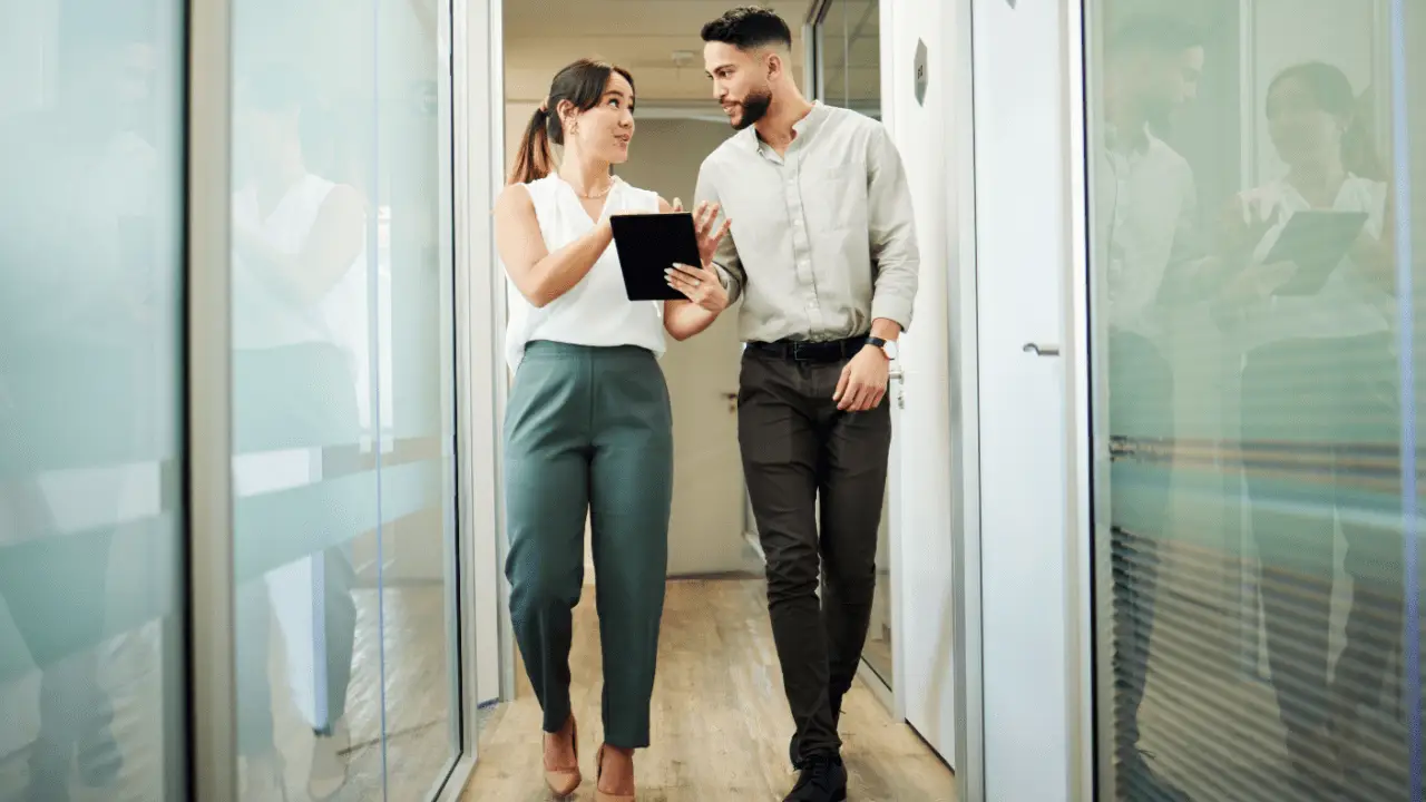 Professional woman and man in business attire walking through office corridor discussing what not to say when you hit a car after accident consultation