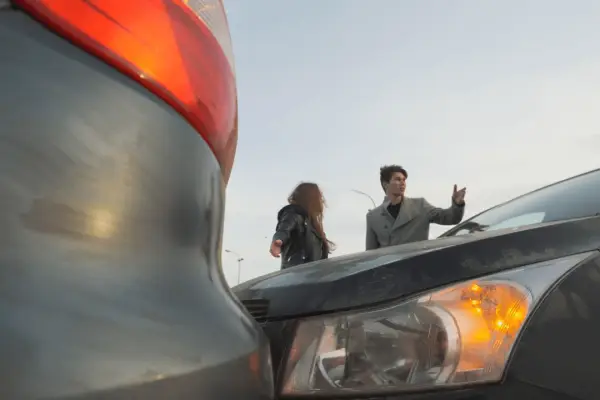 Two people standing near damaged vehicles after a car accident with visible vehicle damage and amber warning lightsTwo people standing near damaged vehicles after a car accident with visible vehicle damage and amber warning lights
