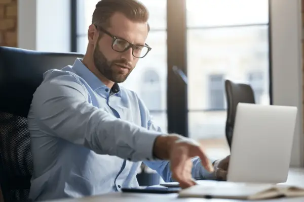 Professional businessman researching how to choose the best car accident lawyer while working on laptop in modern office