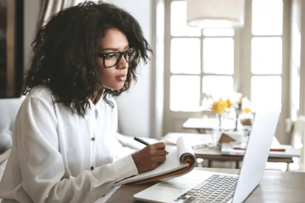 Professional woman researching qualities of the best car accident lawyer while taking notes at laptop in bright home office