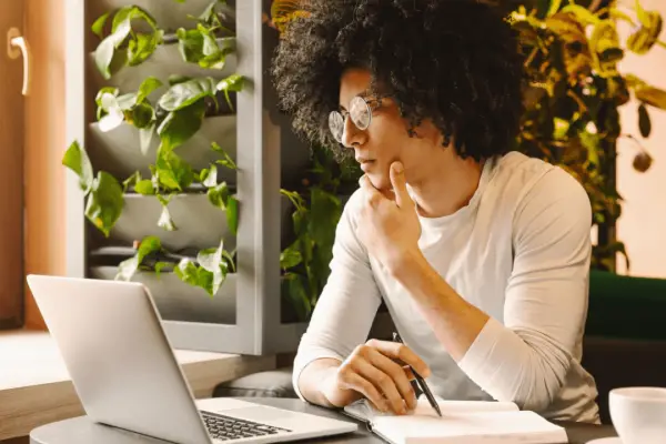 Young man preparing questions to ask a car accident attorney while taking notes at laptop in bright home office