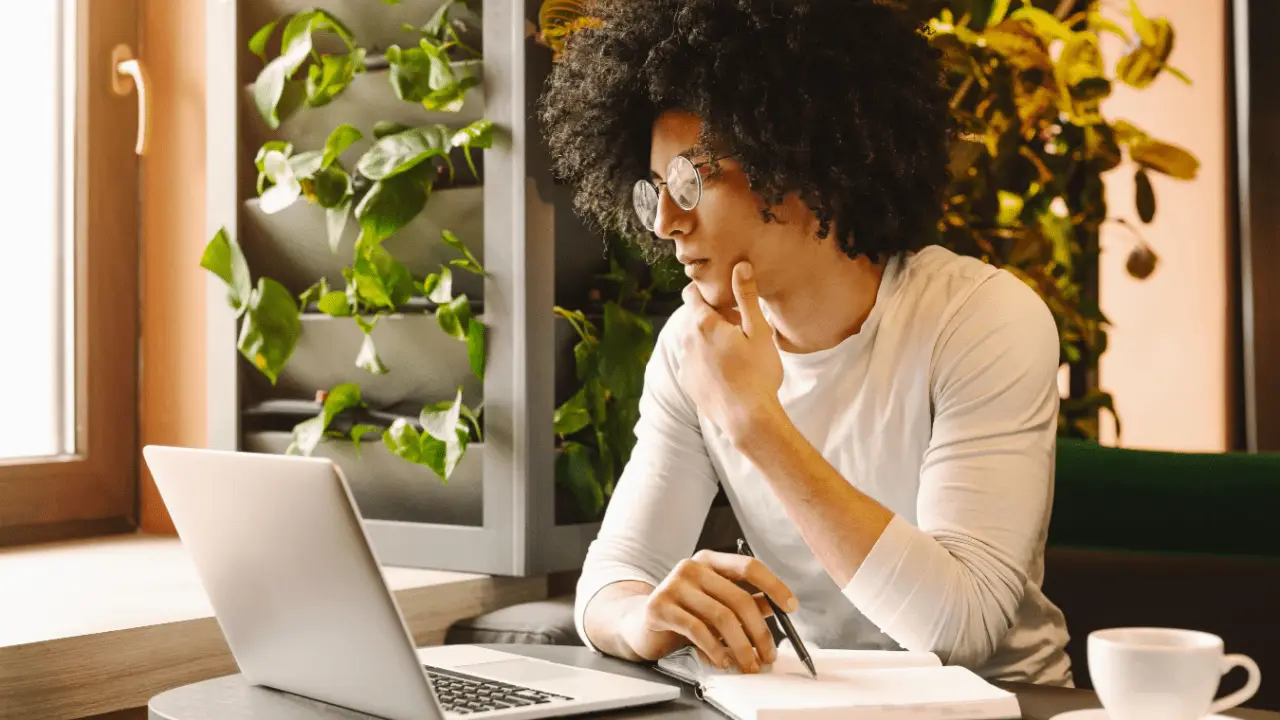 Young man preparing questions to ask a car accident attorney while taking notes at laptop in bright home office