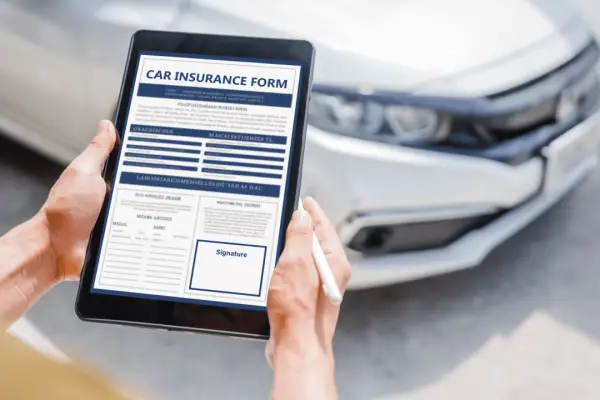 Person reviewing car insurance form on tablet with vehicle in background - what happens if someone sues you for more than your insurance covers