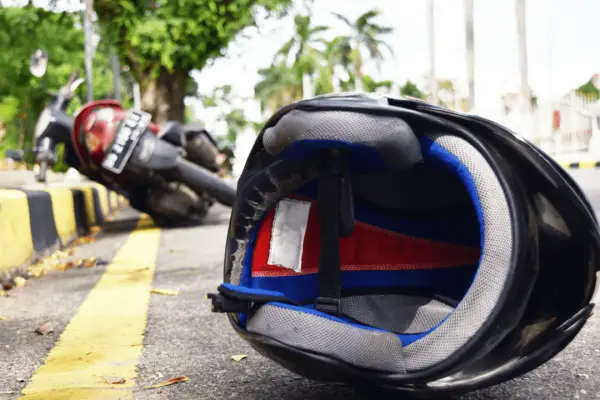 Damaged motorcycle helmet on road after accident showing why understanding how long does a motorcycle accident settlement take is crucial for injury victims