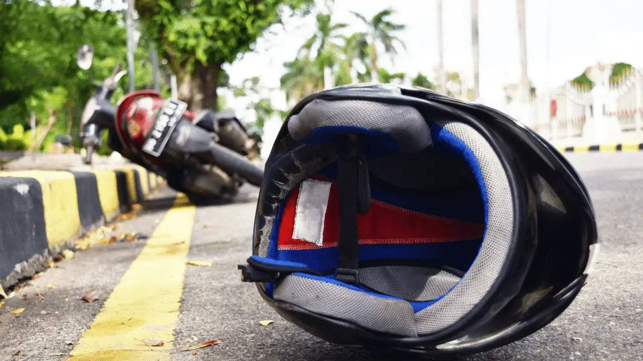 Damaged motorcycle helmet on road after accident showing why understanding how long does a motorcycle accident settlement take is crucial for injury victims