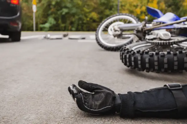 Motorcycle accident scene showing reasons why you need a motorcycle accident lawyer with crashed bike and rider glove on road