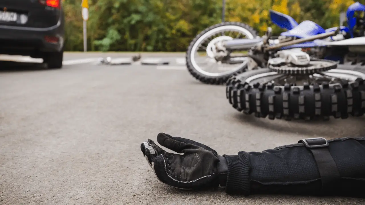 Motorcycle accident scene showing reasons why you need a motorcycle accident lawyer with crashed bike and rider glove on road