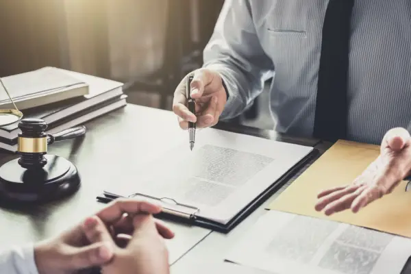 Lawyer discussing how much can you claim for personal injury while client signs legal documents at law office desk with gavel and scales of justice