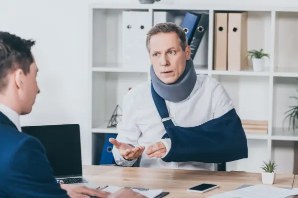 Injured man with neck brace and arm sling consulting lawyer about what injuries pay the most compensation