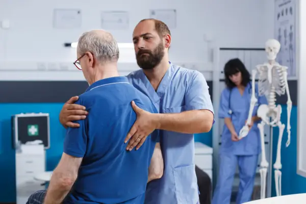 Doctor examining elderly patient's back pain after car accident to determine compensation-worthy injuries