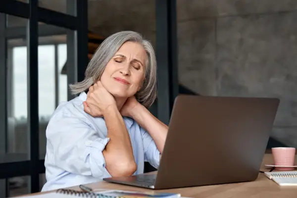 Woman experiencing neck pain at desk wondering what is a typical amount of pain and suffering compensation