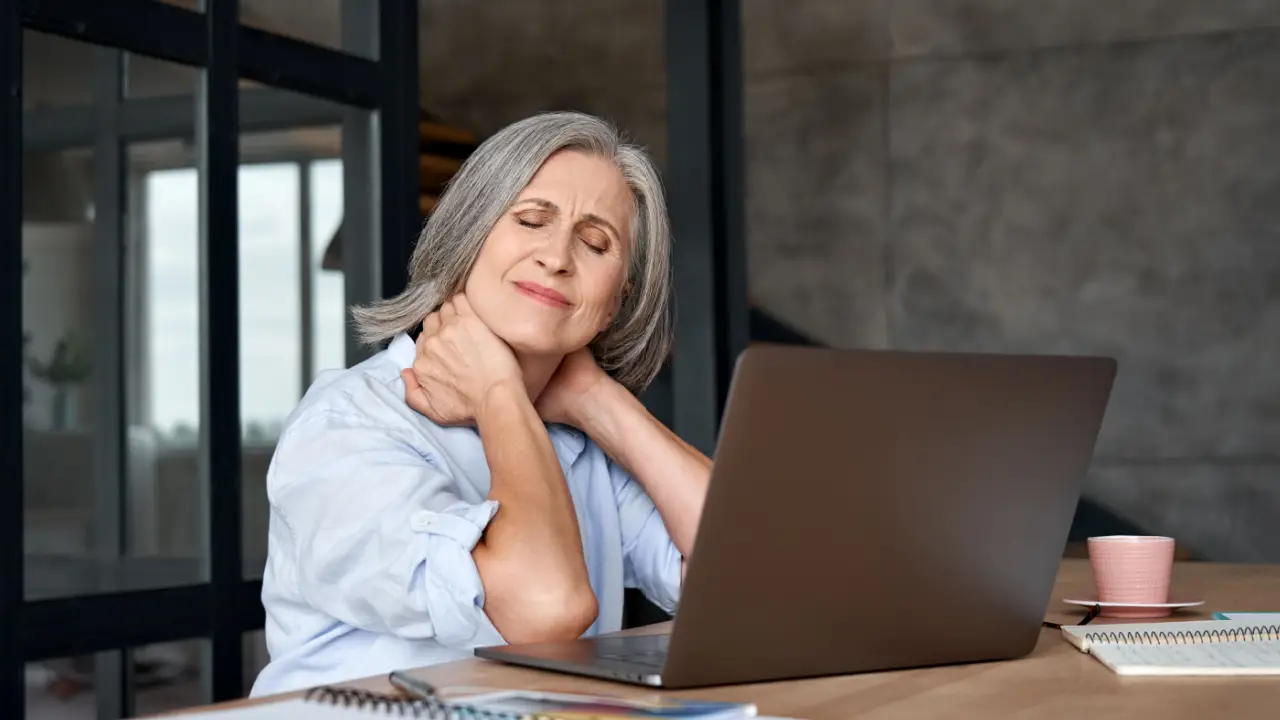 Woman experiencing neck pain at desk wondering what is a typical amount of pain and suffering compensation