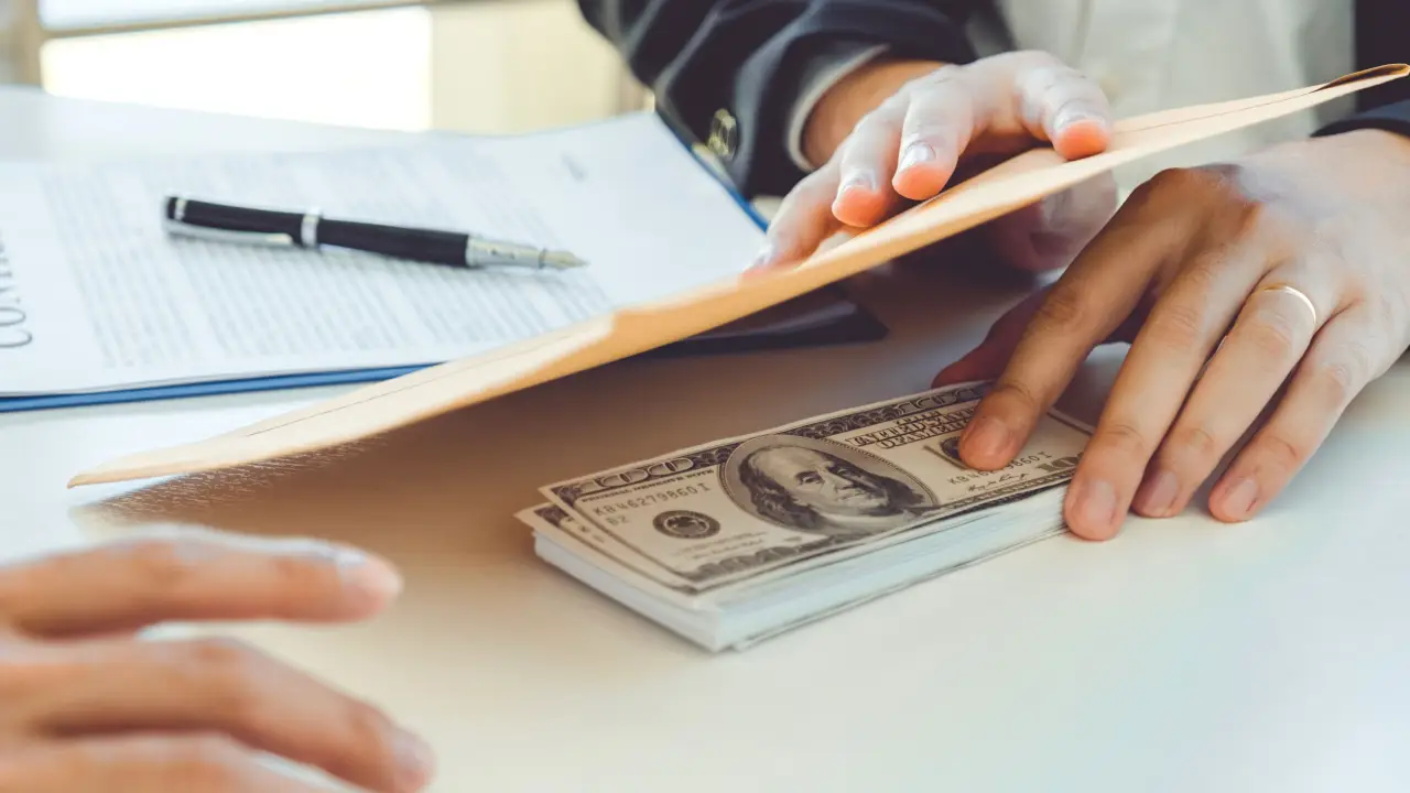 Hands holding legal documents with cash showing how to get the most compensation from a car accident settlement