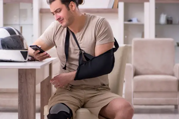 Injured motorcyclist with arm sling and leg brace at home considering how much are most motorcycle accident settlements worth