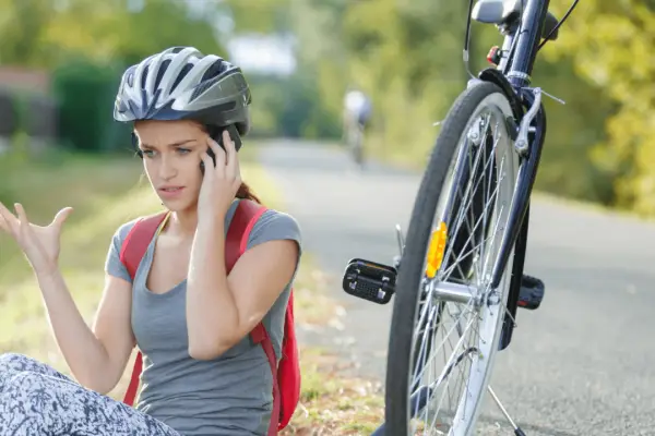Female cyclist wearing helmet sitting on ground after bike crash calling for help showing do bicycle helmets protect the head in a crash