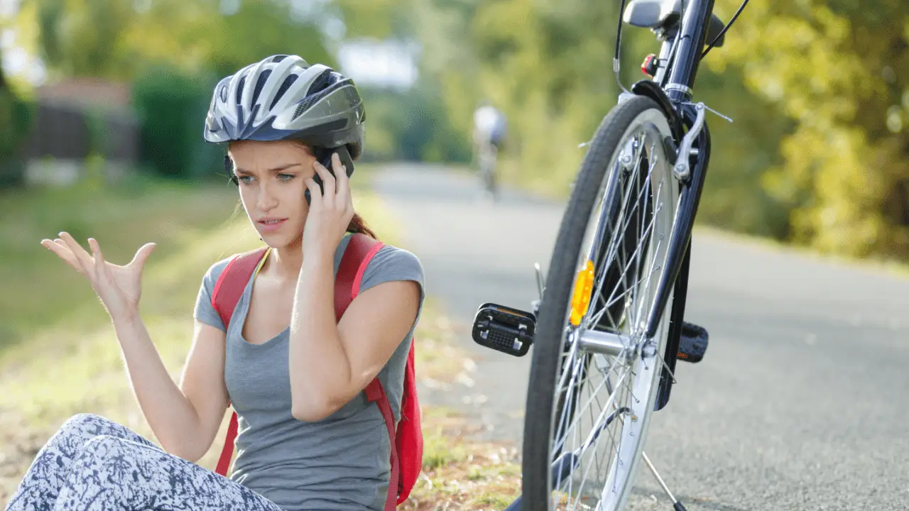 Female cyclist wearing helmet sitting on ground after bike crash calling for help showing do bicycle helmets protect the head in a crash