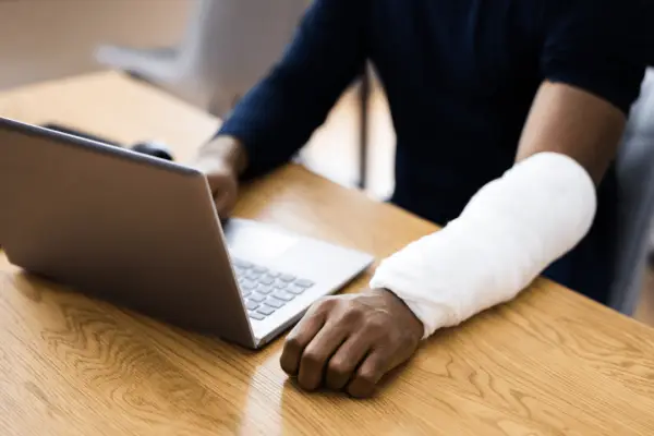 Person with white arm cast using laptop at desk researching how do i find an austin bicycle accident lawyer