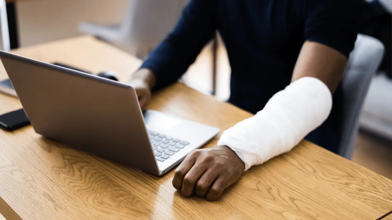 Person with white arm cast using laptop at desk researching how do i find an austin bicycle accident lawyer