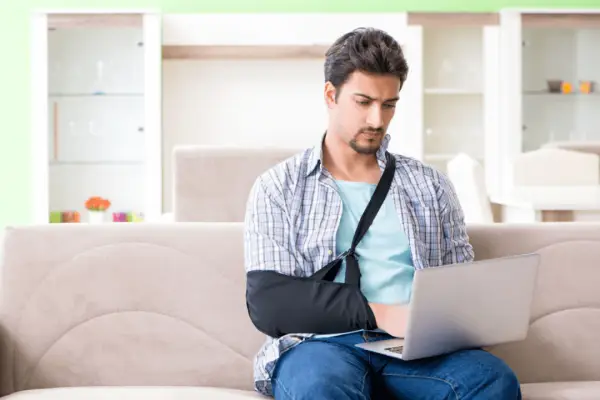 Injured man with arm in sling using laptop at home researching how to choose the best bicycle accident lawyer