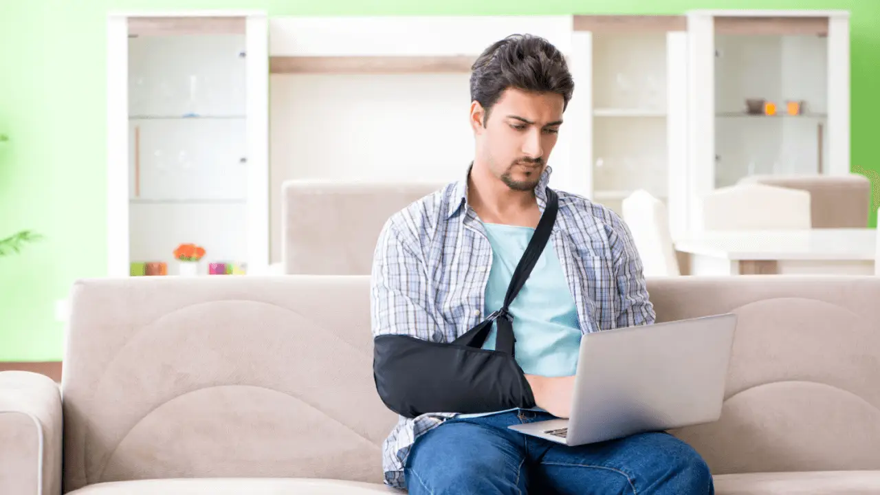 Injured man with arm in sling using laptop at home researching how to choose the best bicycle accident lawyer