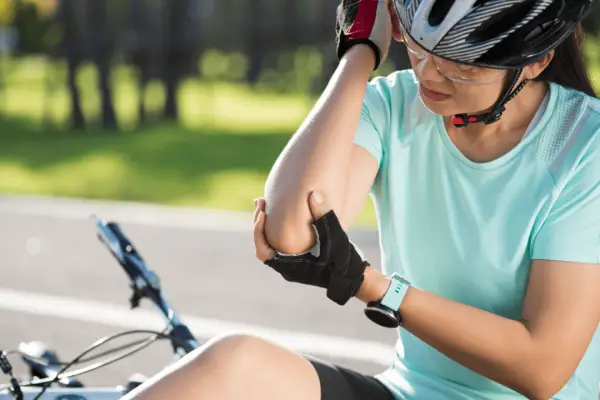 Injured cyclist wearing helmet holding injured arm after bike accident illustrating is a bicycle safer than a car safety comparison