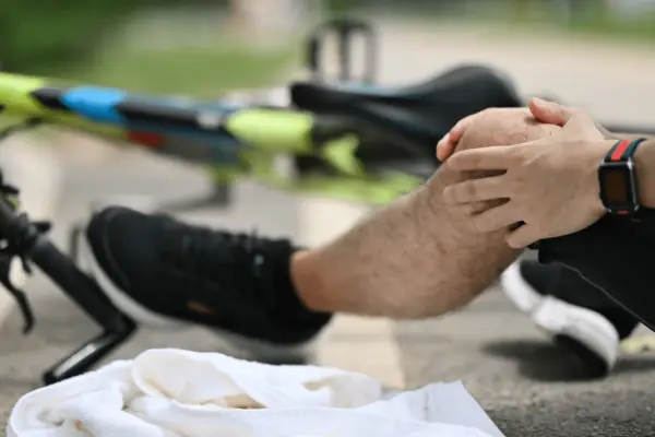 Cyclist holding injured knee after bicycle accident causes fall on road with bike in background