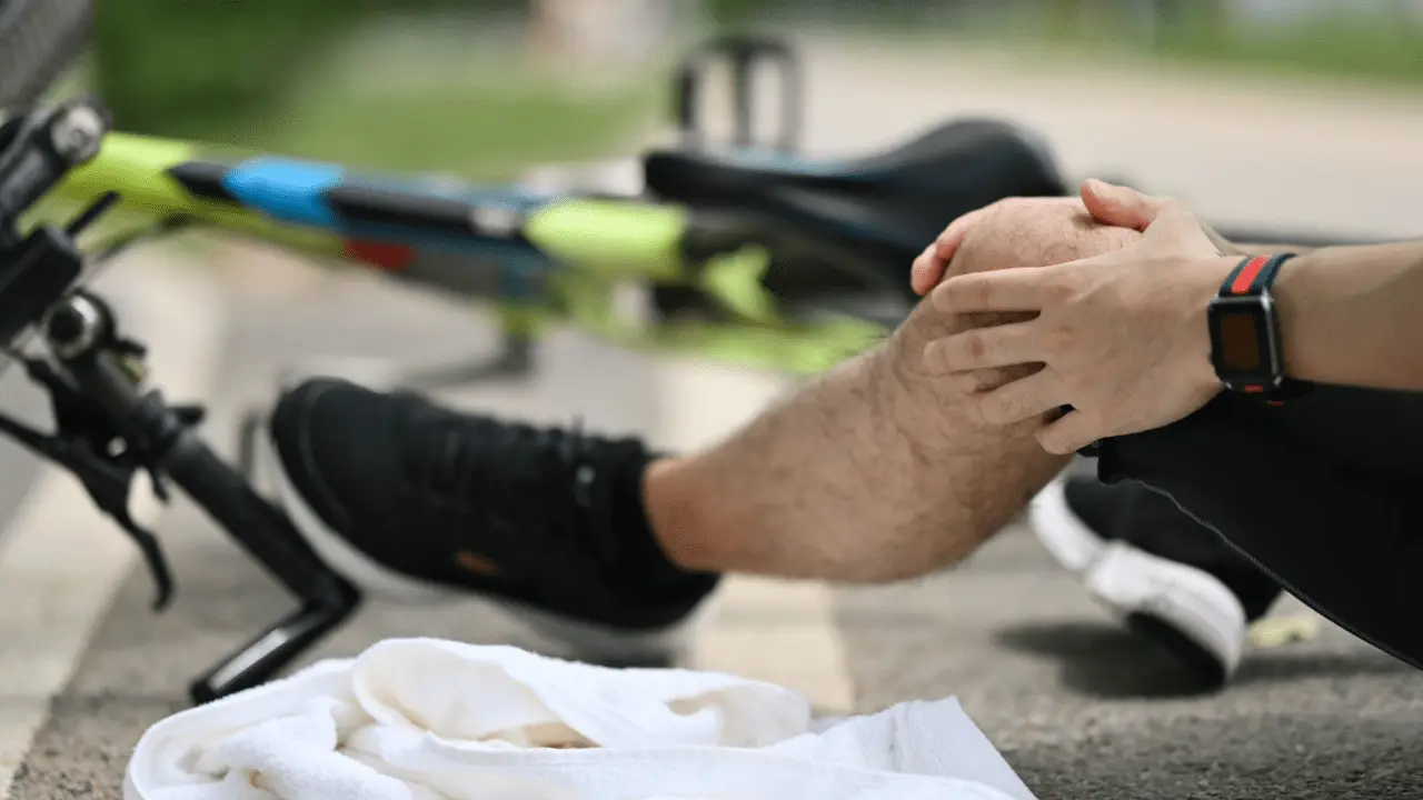 Cyclist holding injured knee after bicycle accident causes fall on road with bike in background