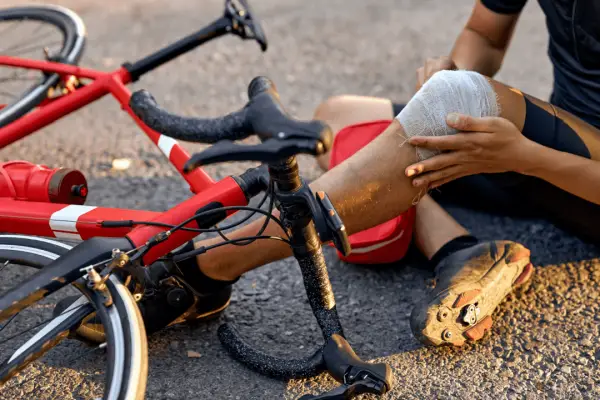 Injured cyclist with bandaged knee demonstrating what is the most common injury in cycling after falling from red road bike
