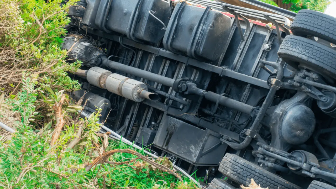 Determining fault in truck accidents scene with overturned commercial vehicle showing undercarriage and mechanical damage in roadside grass