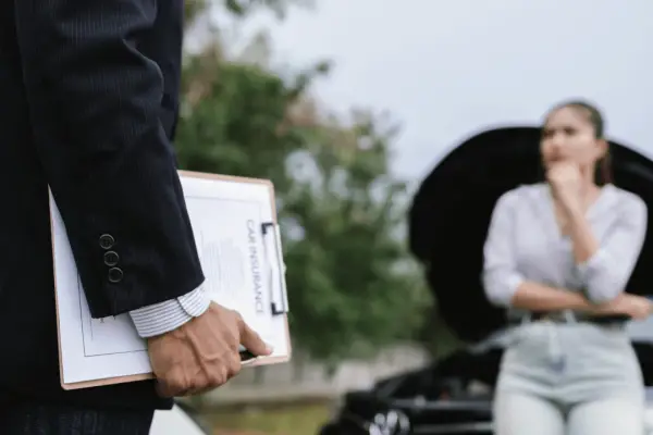 Insurance claim not at fault adjuster holding car insurance clipboard with concerned woman standing near damaged vehicle