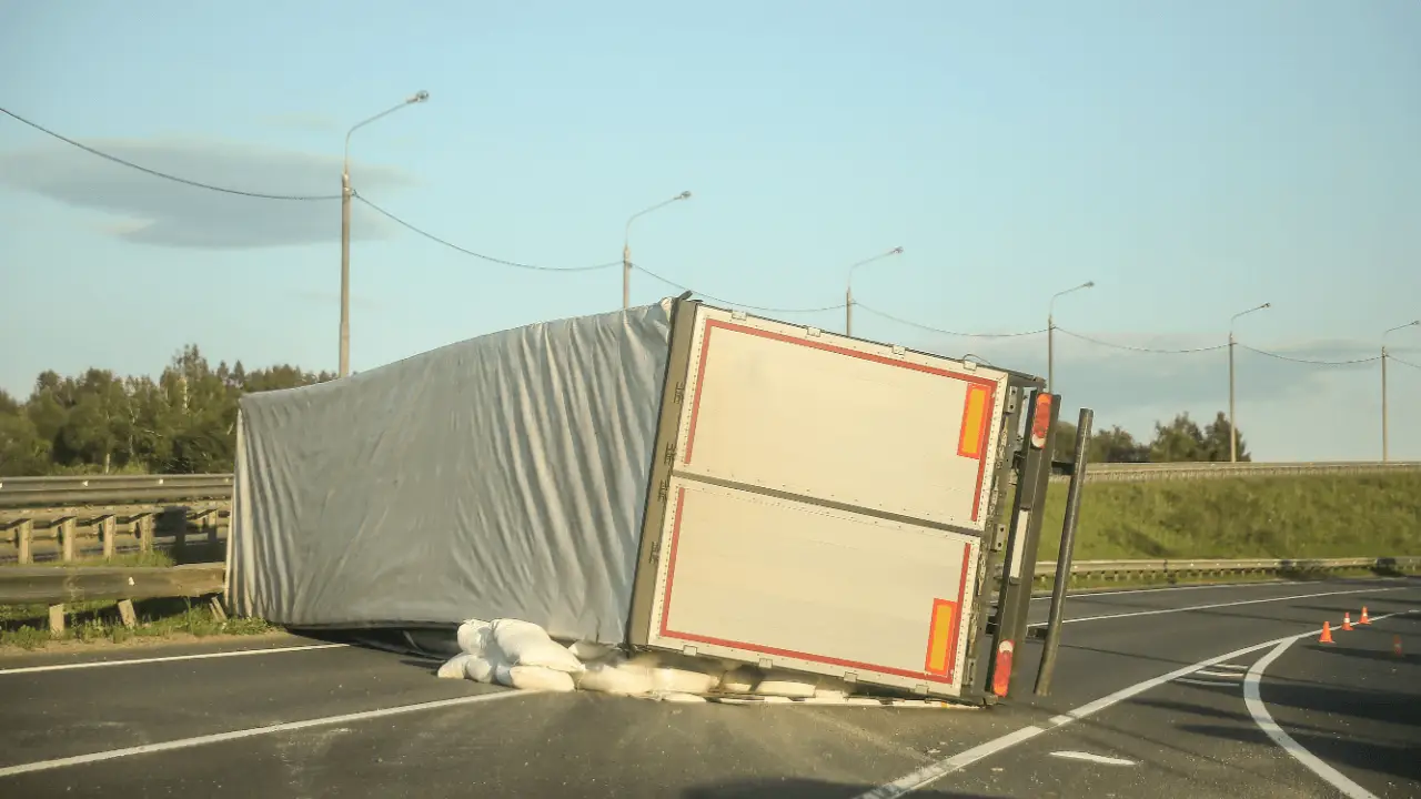 Truck accident fault and liability scene with overturned cargo trailer and spilled freight on highway with traffic cones
