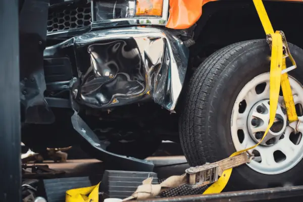 Truck accident liability scene with severely damaged vehicle showing crushed front fender and hood secured by yellow straps on tow truck
