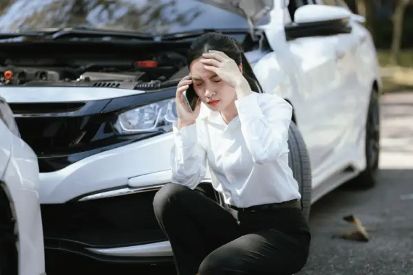 Woman on phone after car accident crouching beside damaged vehicle knowing who to call after a car accident