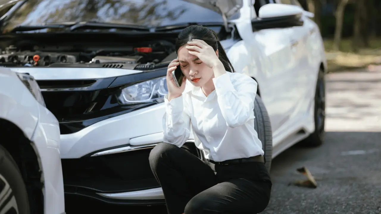 Woman on phone after car accident crouching beside damaged vehicle knowing who to call after a car accident